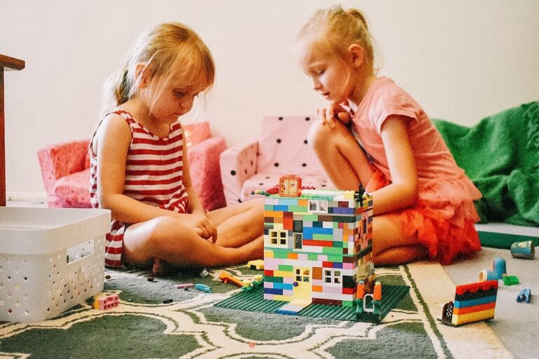 Two young girls working together to build a rainbow coloured lego house.