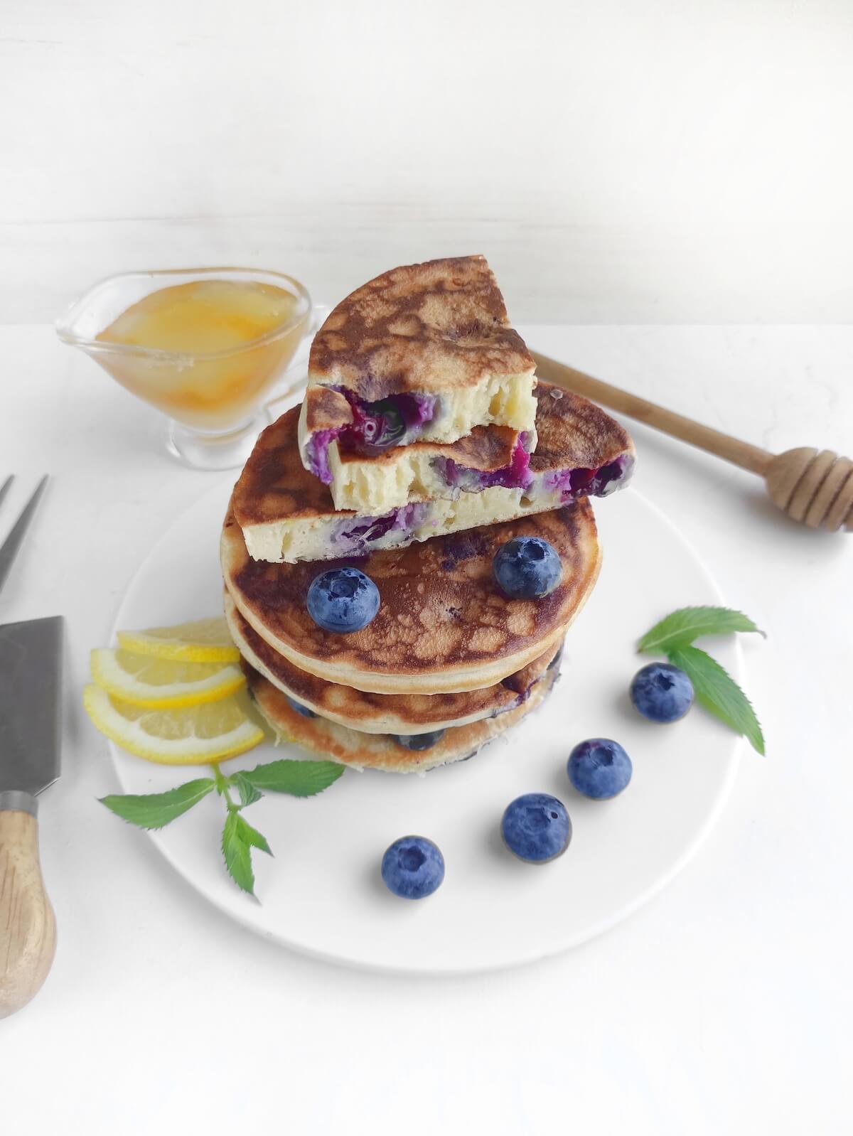 stack of blueberry lemon pancakes on white plate with top pancake cut into.