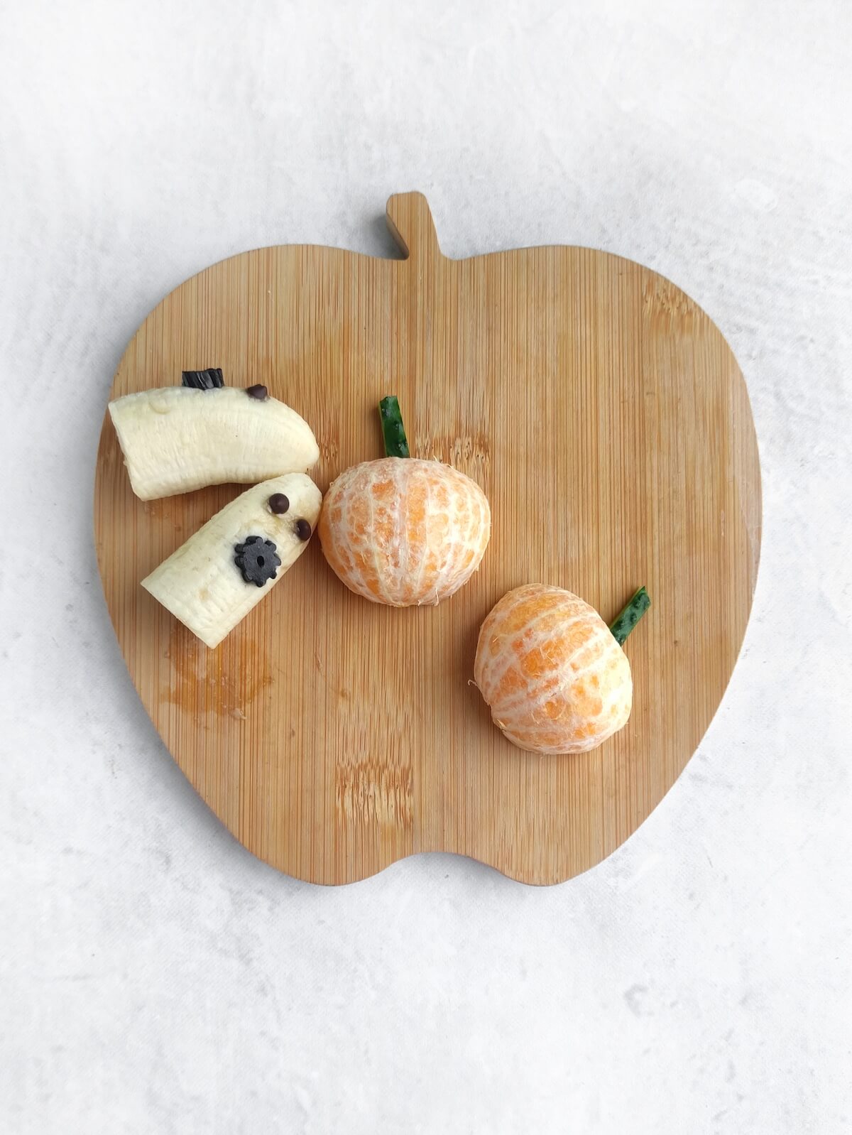 apple shaped chopping board with bananas and mandarines.